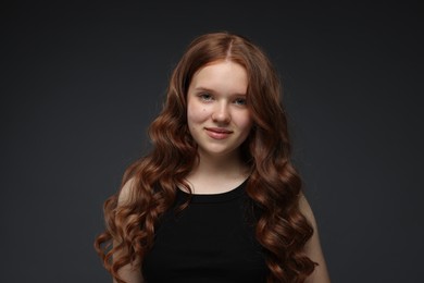 Photo of Portrait of beautiful teenage girl with healthy wavy hair on dark grey background