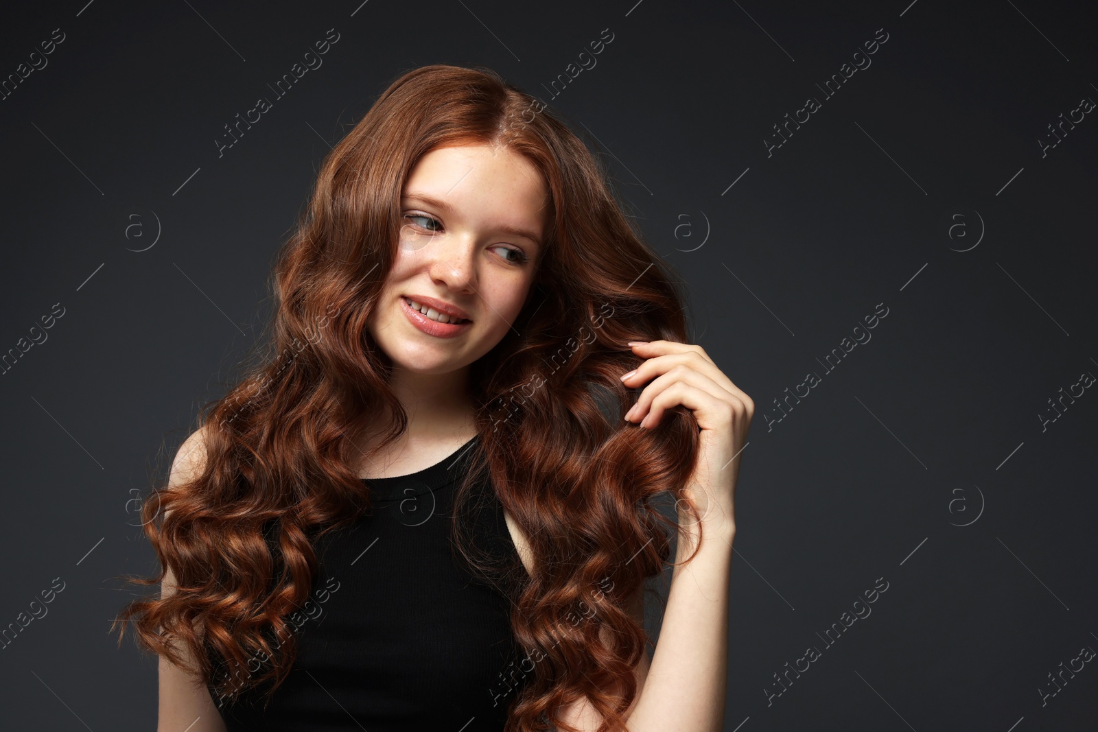 Smiling teenage girl with healthy wavy hair on dark grey background. Space for text Photo of Smiling teenage girl with healthy wavy hair on dark grey background. Space for text