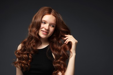 Photo of Smiling teenage girl with healthy wavy hair on dark grey background. Space for text