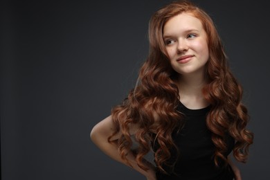 Photo of Portrait of beautiful teenage girl with healthy wavy hair on dark grey background. Space for text