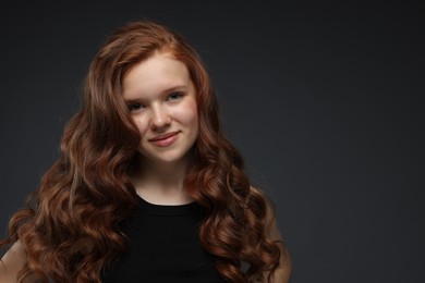 Photo of Portrait of beautiful teenage girl with healthy wavy hair on dark grey background. Space for text