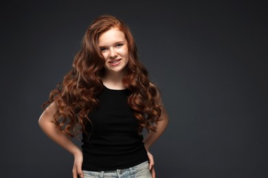 Photo of Portrait of smiling teenage girl with healthy wavy hair on dark grey background. Space for text