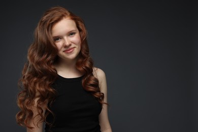 Photo of Portrait of beautiful teenage girl with healthy wavy hair on dark grey background. Space for text