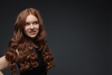 Photo of Smiling teenage girl with healthy wavy hair on dark grey background. Space for text