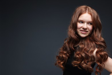 Photo of Smiling teenage girl with healthy wavy hair on dark grey background. Space for text
