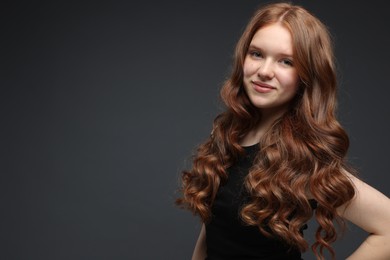Photo of Portrait of beautiful teenage girl with healthy wavy hair on dark grey background. Space for text