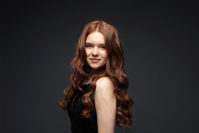 Photo of Portrait of beautiful teenage girl with healthy wavy hair on dark grey background