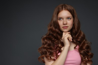 Photo of Beautiful teenage girl with healthy wavy hair on dark grey background. Space for text