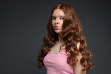 Photo of Portrait of beautiful teenage girl with healthy wavy hair on dark grey background. Space for text