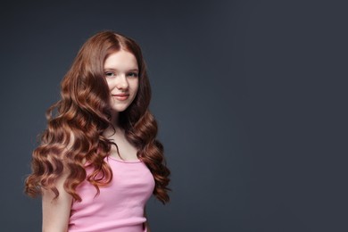 Photo of Portrait of beautiful teenage girl with healthy wavy hair on dark grey background. Space for text