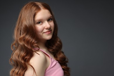 Photo of Portrait of beautiful teenage girl with healthy wavy hair on dark grey background. Space for text