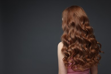 Photo of Teenage girl with healthy wavy hair on dark grey background, back view. Space for text