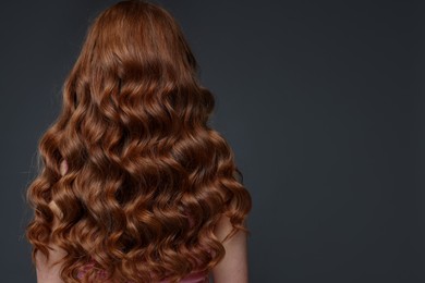 Photo of Teenage girl with healthy wavy hair on dark grey background, back view. Space for text
