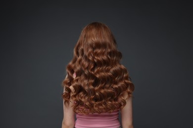 Photo of Teenage girl with healthy wavy hair on dark grey background, back view