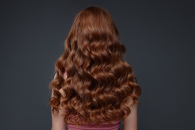 Photo of Teenage girl with healthy wavy hair on dark grey background, back view