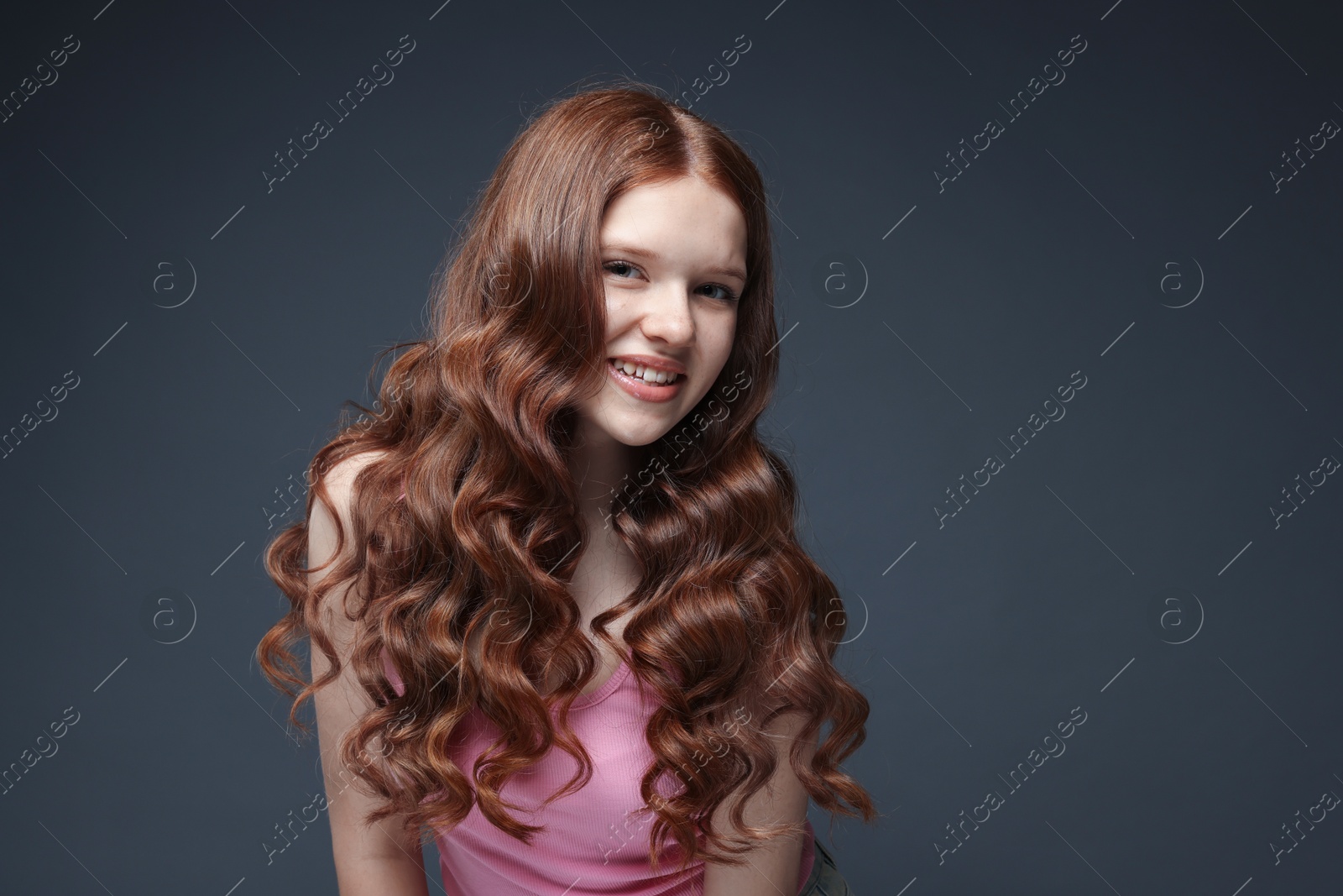 Portrait of smiling teenage girl with healthy wavy hair on dark grey background Photo of Portrait of smiling teenage girl with healthy wavy hair on dark grey background