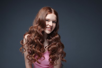 Photo of Portrait of smiling teenage girl with healthy wavy hair on dark grey background