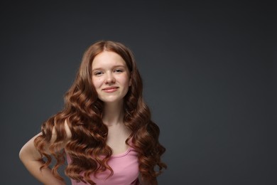 Photo of Portrait of beautiful teenage girl with healthy wavy hair on dark grey background. Space for text