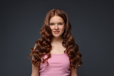 Photo of Portrait of beautiful teenage girl with healthy wavy hair on dark grey background