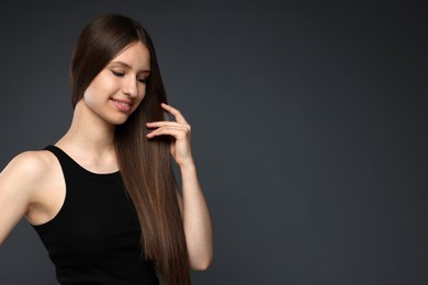 Photo of Smiling teenage girl with healthy long hair on dark grey background. Space for text
