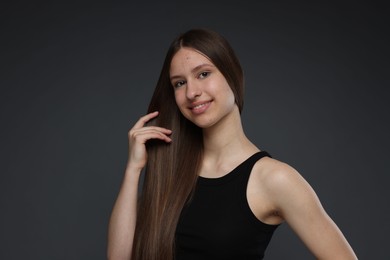 Photo of Portrait of smiling teenage girl with healthy long hair on dark grey background