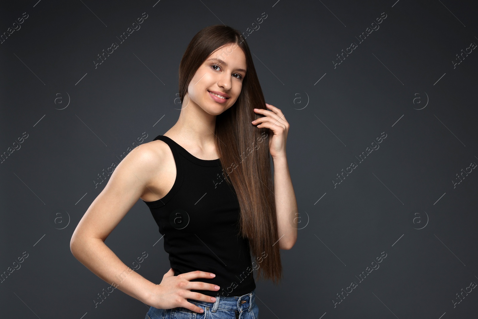 Portrait of smiling teenage girl with healthy long hair on dark grey background Photo of Portrait of smiling teenage girl with healthy long hair on dark grey background