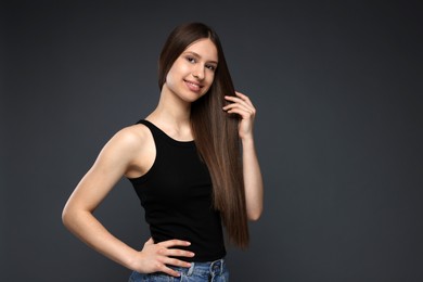 Photo of Portrait of smiling teenage girl with healthy long hair on dark grey background