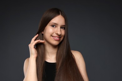 Photo of Portrait of smiling teenage girl with healthy long hair on dark grey background