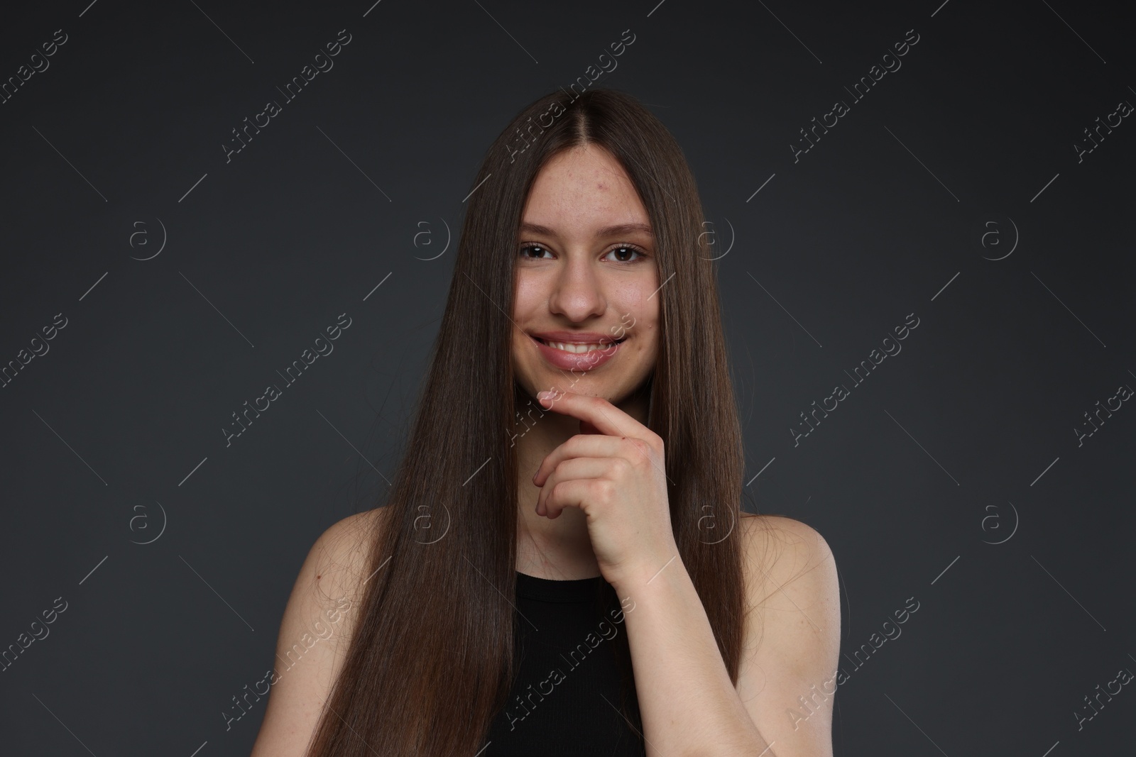 Portrait of smiling teenage girl with healthy long hair on dark grey background Photo of Portrait of smiling teenage girl with healthy long hair on dark grey background