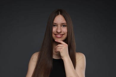Photo of Portrait of smiling teenage girl with healthy long hair on dark grey background