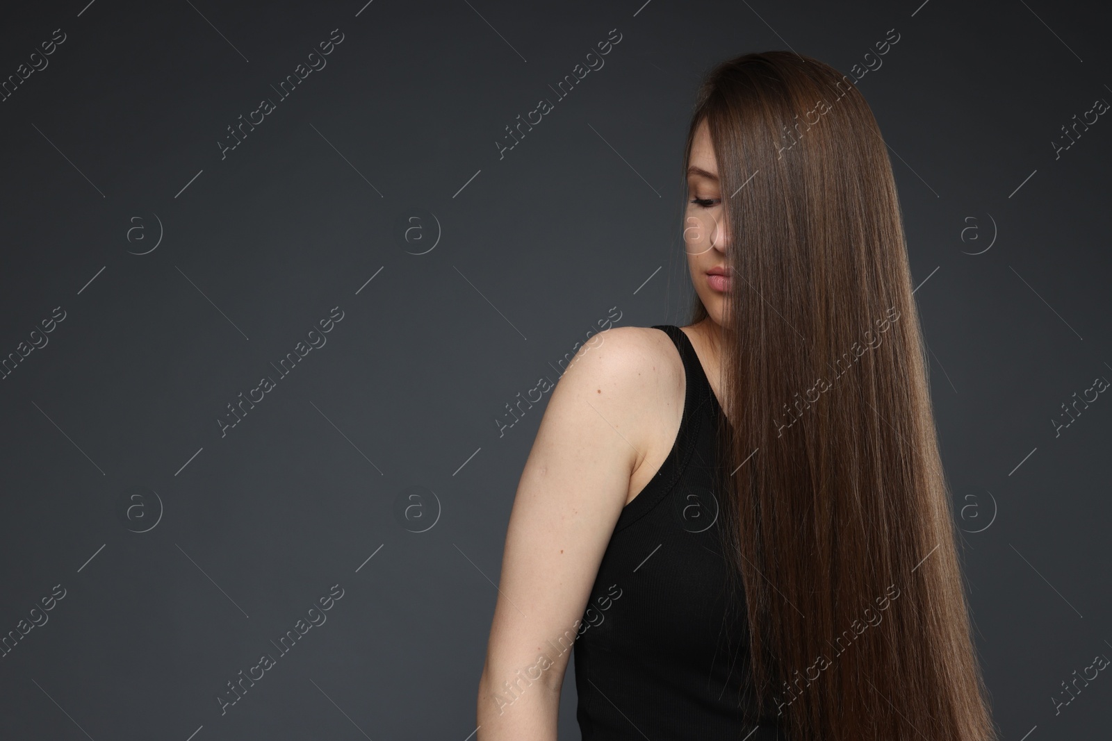 Teenage girl with healthy long hair on dark grey background. Space for text Photo of Teenage girl with healthy long hair on dark grey background. Space for text