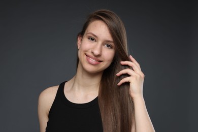 Photo of Portrait of smiling teenage girl with healthy long hair on dark grey background