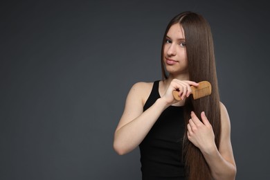 Photo of Beautiful teenage girl brushing her healthy long hair on dark grey background. Space for text