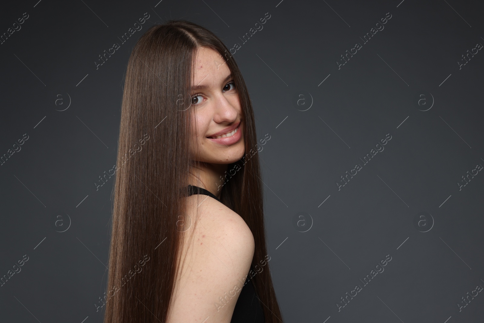 Portrait of smiling teenage girl with healthy long hair on dark grey background. Space for text Photo of Portrait of smiling teenage girl with healthy long hair on dark grey background. Space for text