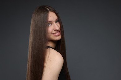 Photo of Portrait of smiling teenage girl with healthy long hair on dark grey background. Space for text