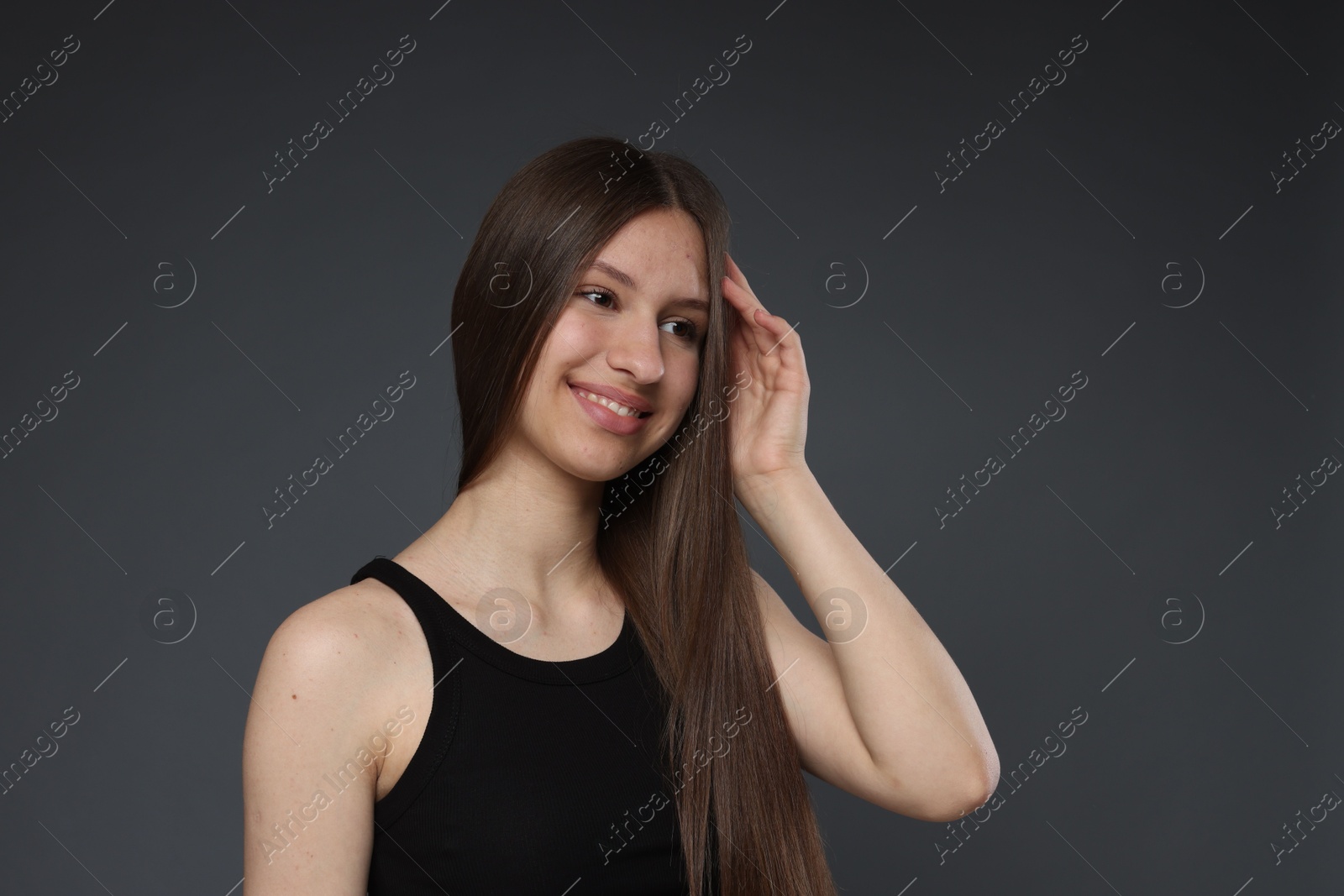 Portrait of smiling teenage girl with healthy long hair on dark grey background Photo of Portrait of smiling teenage girl with healthy long hair on dark grey background