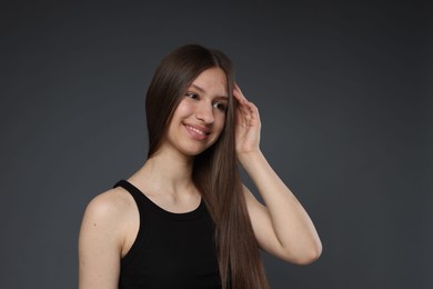 Photo of Portrait of smiling teenage girl with healthy long hair on dark grey background