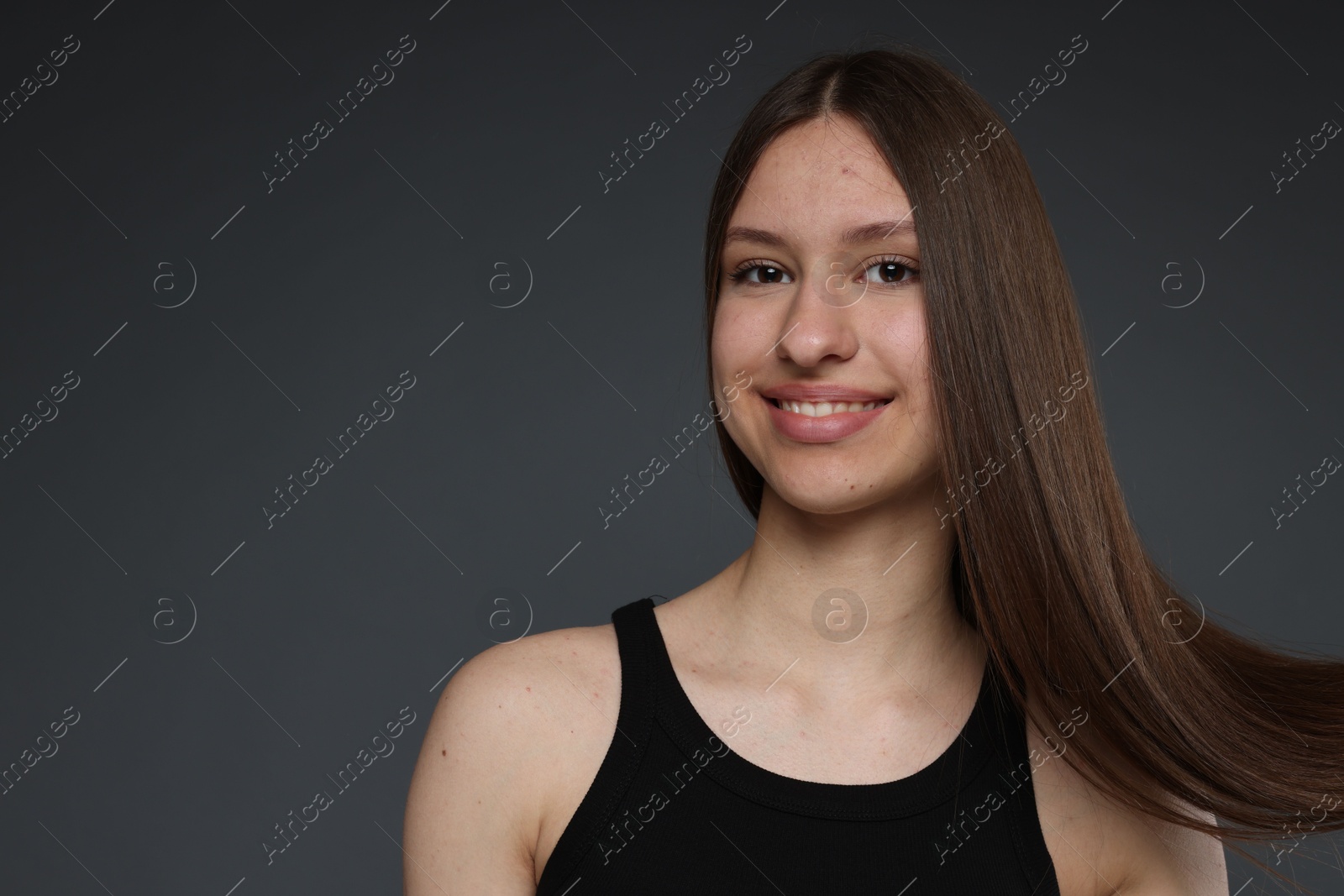 Portrait of smiling teenage girl with healthy long hair on dark grey background. Space for text Photo of Portrait of smiling teenage girl with healthy long hair on dark grey background. Space for text