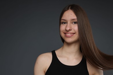 Photo of Portrait of smiling teenage girl with healthy long hair on dark grey background. Space for text