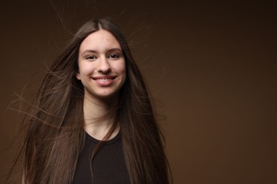 Photo of Portrait of smiling teenage girl with healthy long hair on brown background. Space for text