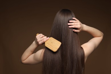 Photo of Teenage girl brushing her healthy long hair on brown background, back view