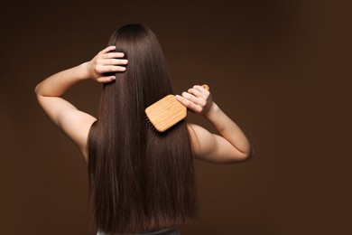 Photo of Teenage girl brushing her healthy long hair on brown background, back view. Space for text