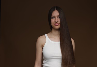 Photo of Portrait of beautiful teenage girl with healthy long hair on brown background. Space for text