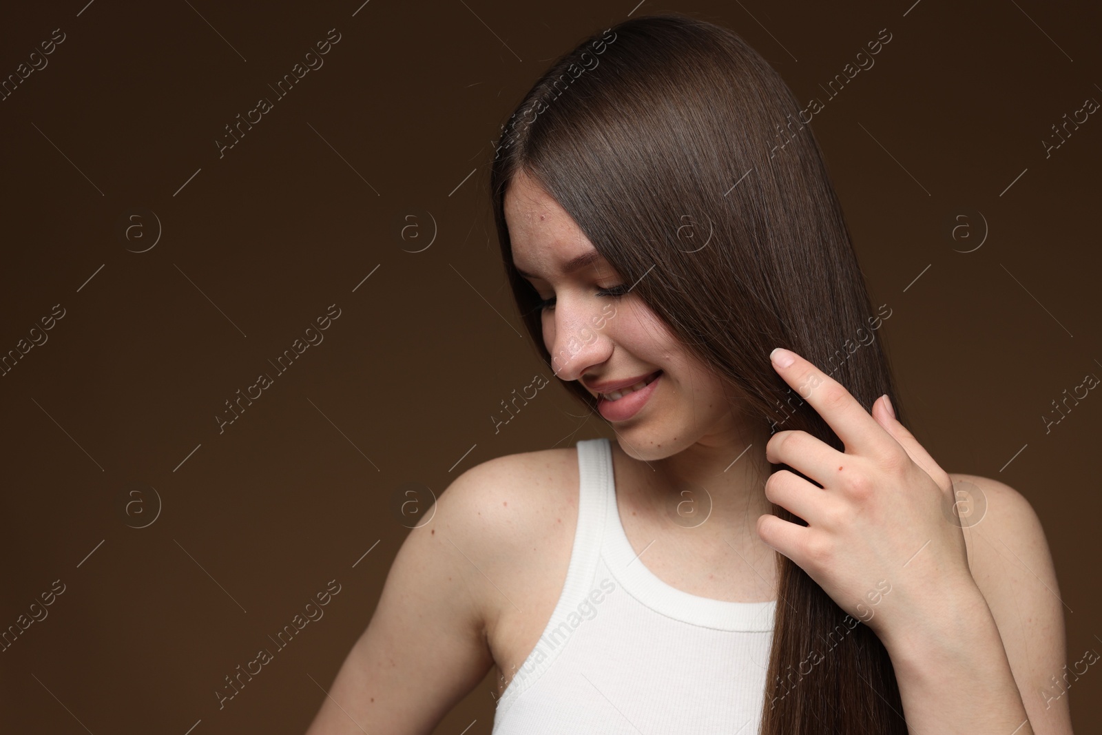 Smiling teenage girl with healthy long hair on brown background. Space for text Photo of Smiling teenage girl with healthy long hair on brown background. Space for text