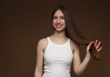 Photo of Portrait of smiling teenage girl with healthy long hair on brown background. Space for text