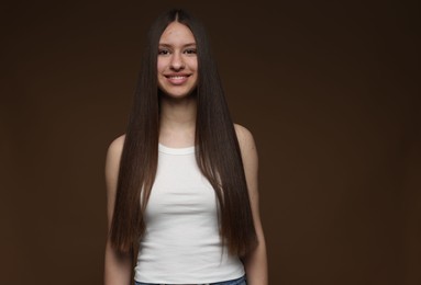 Photo of Portrait of smiling teenage girl with healthy long hair on brown background