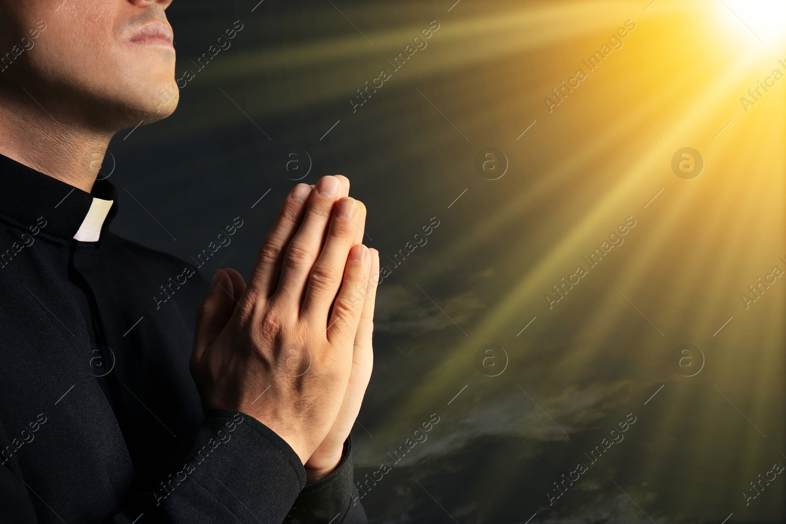 Priest illuminated by holy light praying against beautiful sky, closeup Image of Priest illuminated by holy light praying against beautiful sky, closeup