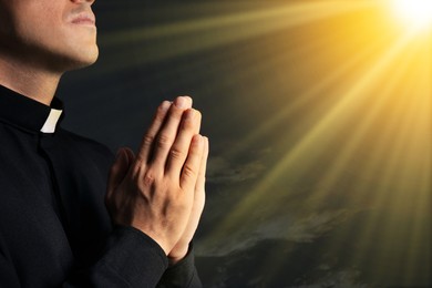 Image of Priest illuminated by holy light praying against beautiful sky, closeup