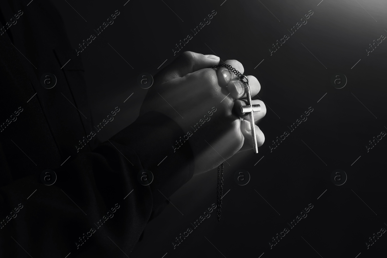 Priest with cross illuminated by holy light praying, closeup. Black-and-white effect Image of Priest with cross illuminated by holy light praying, closeup. Black-and-white effect