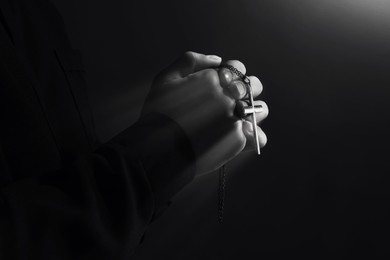 Image of Priest with cross illuminated by holy light praying, closeup. Black-and-white effect